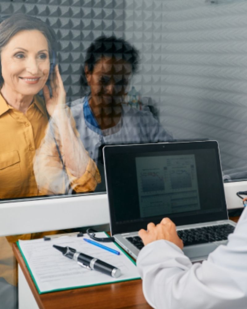 Mobiler Hörservice: Eine lächelnde Frau wird von einer Expertin in entspannter Atmosphäre zu Hause über die Auswahl diskreter Hörgeräte beraten.