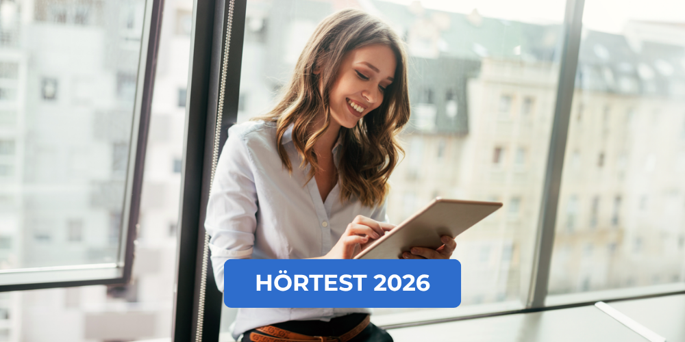 Lächelnde Frau am Fenster informiert sich auf einem Tablet zum Thema Hörtest 2026
