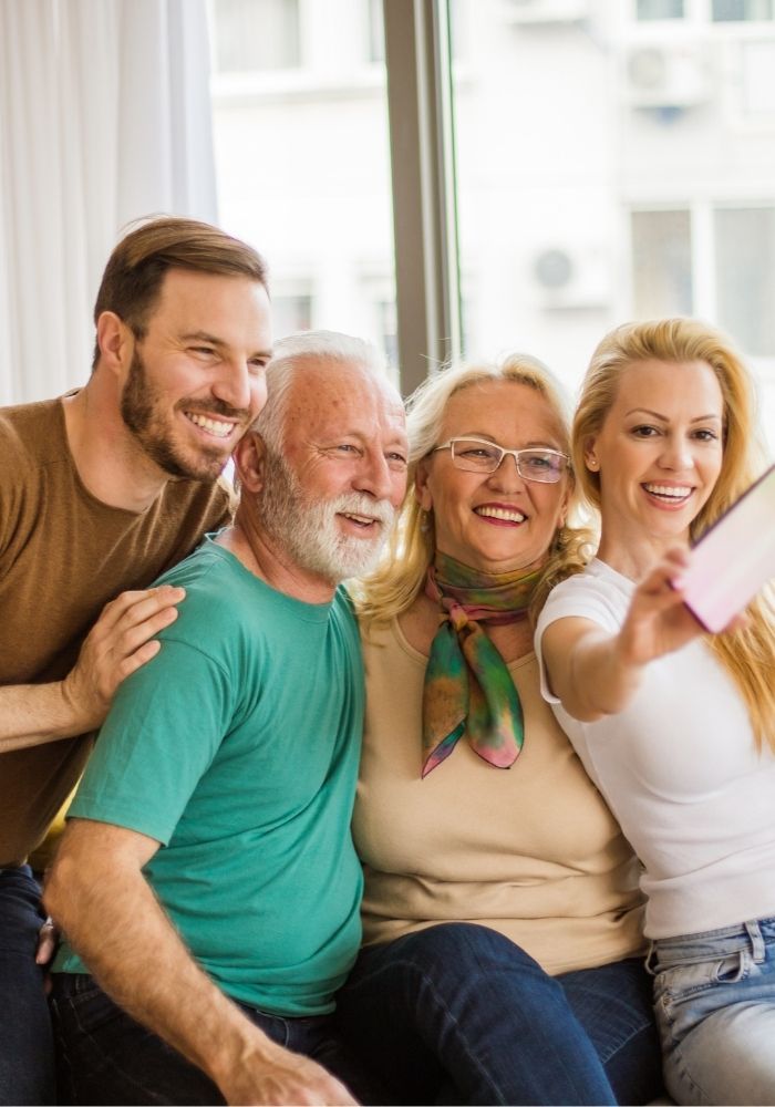 Älteres Paar macht mit erwachsenen Kindern ein fröhliches Selfie – soziale Teilhabe dank gutem Hören kann das Demenzrisiko senken